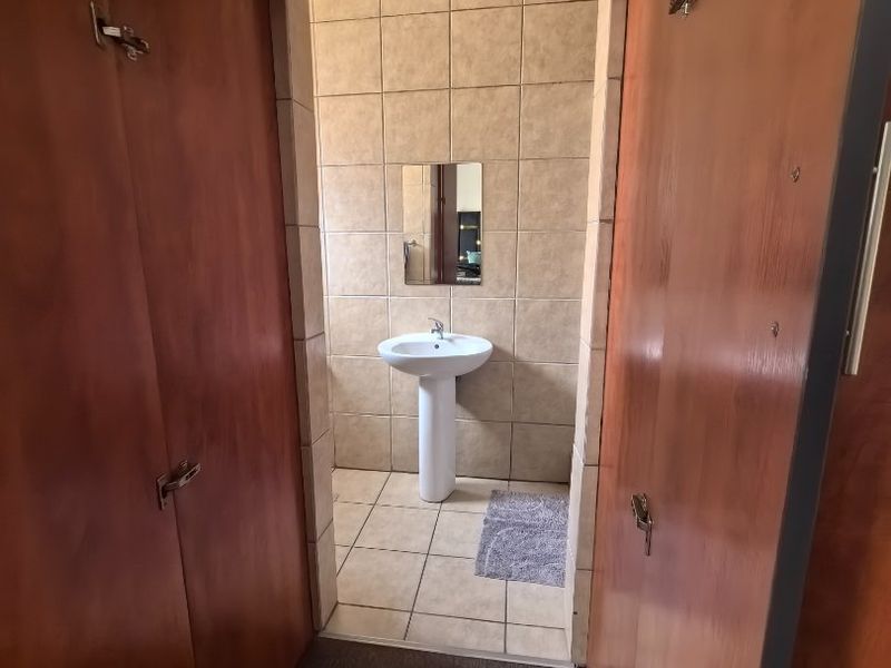 A functional bathroom featuring a pedestal basin, tiled finishes, and built-in wooden cabinetry, offering a clean and practical space.