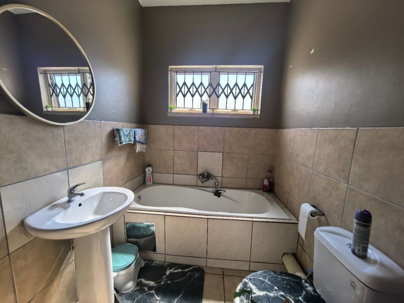 A functional bathroom featuring a pedestal basin, built-in bathtub, and tiled wall finishes, complete with security bars on the window.