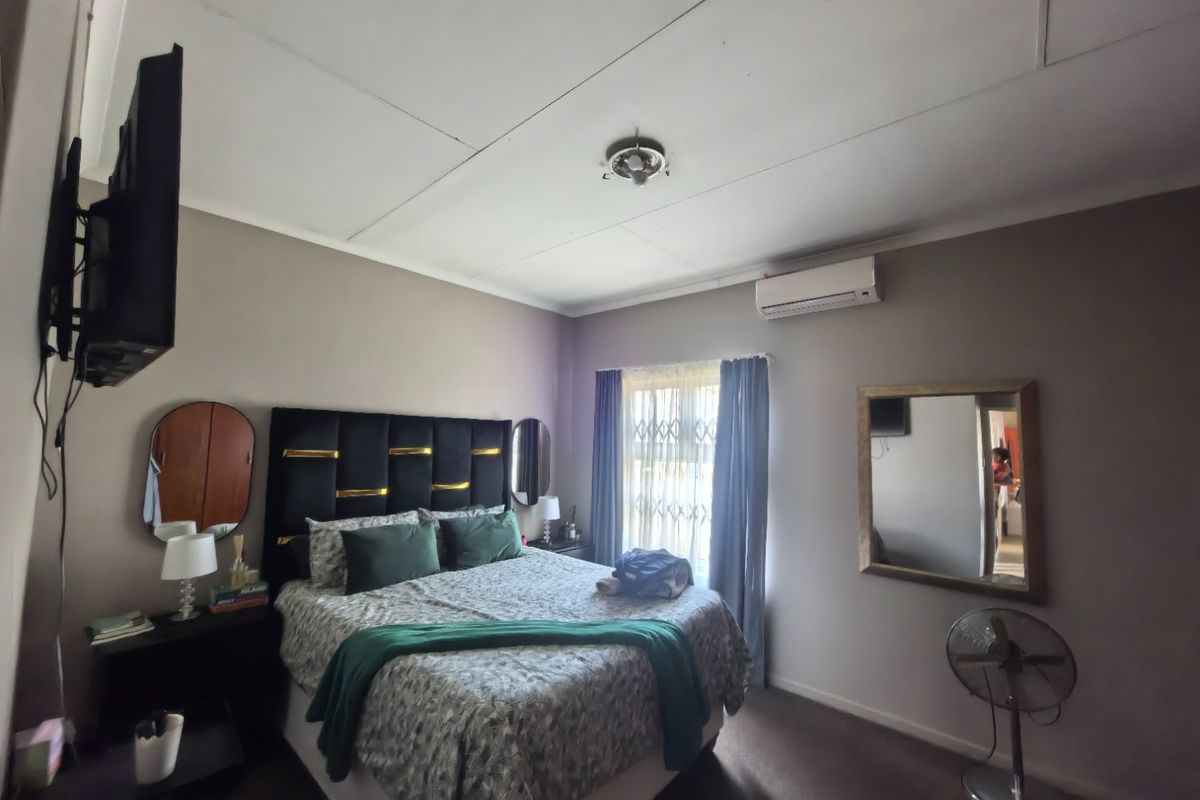 A functional bedroom featuring a wall-mounted air conditioning unit, security gate on the window, and neutral wall finishes.
