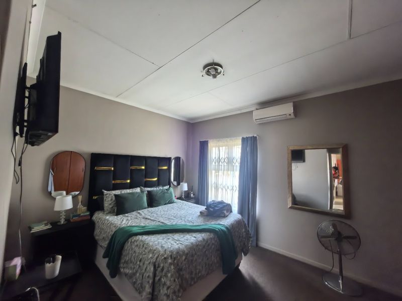 A functional bedroom featuring a wall-mounted air conditioning unit, security gate on the window, and neutral wall finishes.