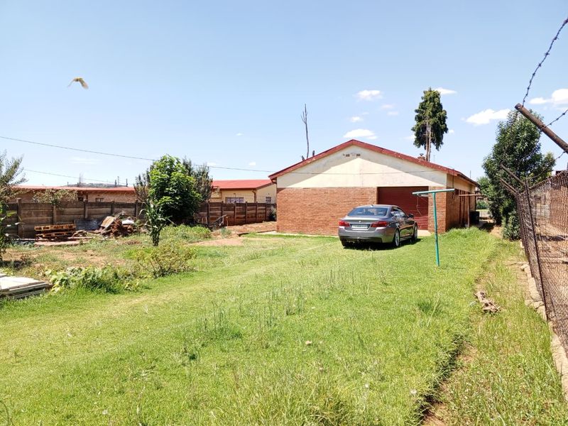 Rear view of the property featuring a brick garage, expansive lawn area, and perimeter boundary walling.