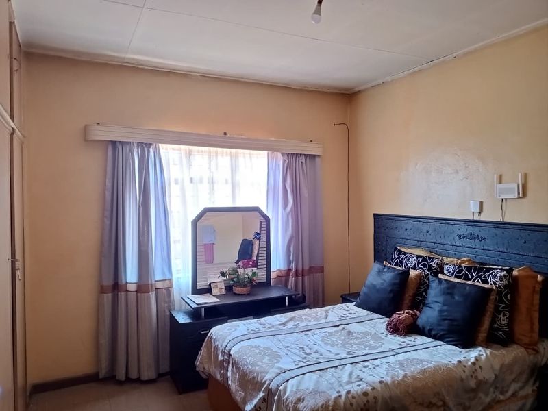 A bedroom featuring a built-in wardrobe and a window with curtain rails, requiring cosmetic updates to the walls and ceiling.
