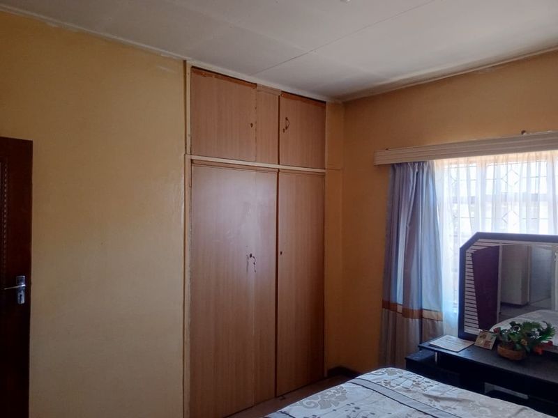 A bedroom featuring built-in wooden cupboards and a window with security bars, offering a functional space with potential for cosmetic updates.
