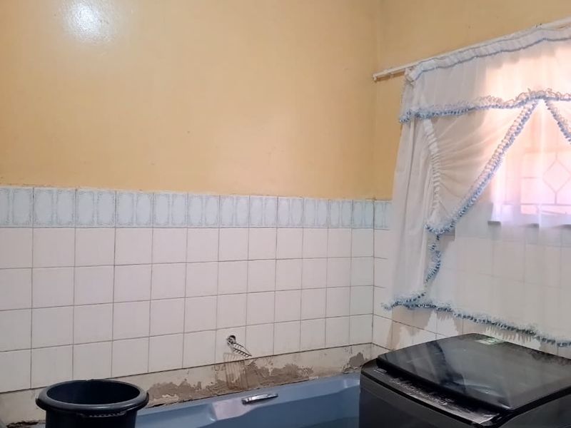 A bathroom featuring a bathtub and wall tiling, currently showing signs of wear including missing tiles and exposed wall areas requiring repair.