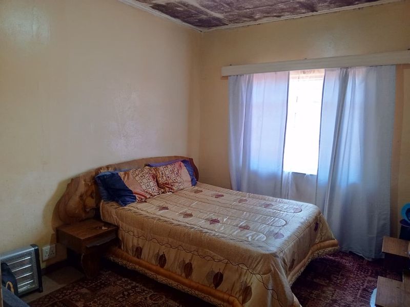 A bedroom featuring a window with a curtain rail, showing signs of ceiling water damage and wall surface deterioration requiring maintenance.