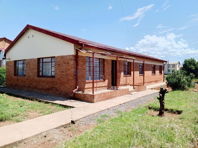 A single-story face brick house featuring a corrugated metal roof, security window bars, and a concrete walkway leading to a covered porch area.