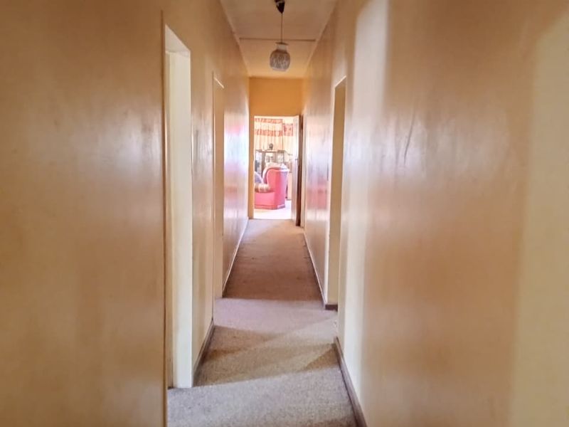 A long, narrow residential hallway featuring carpeted flooring and a central pendant light fixture, providing access to multiple rooms.