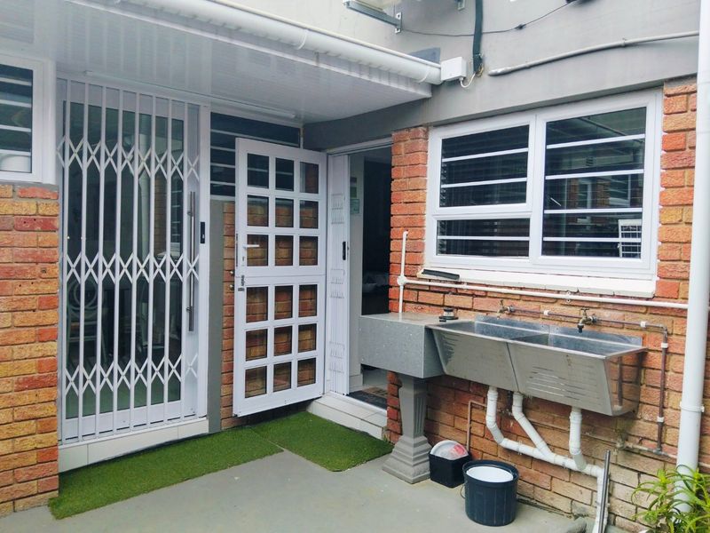 Outdoor laundry area featuring a stainless steel double sink, exposed plumbing, and secure access points with security gates and bars.