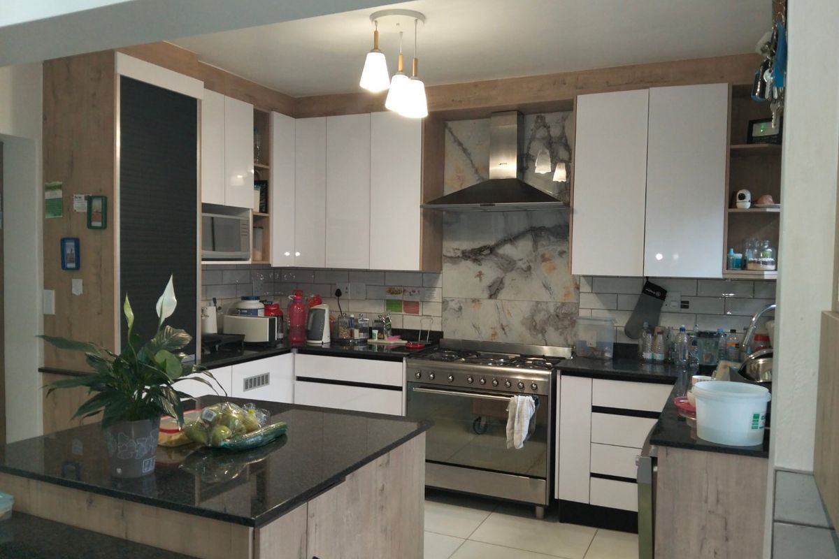 Modern kitchen featuring white and wood-grain cabinetry, stone countertops, a central island, and a stainless steel gas stove with a decorative splashback.