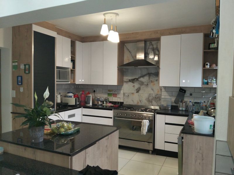 Modern kitchen featuring white and wood-grain cabinetry, stone countertops, a central island, and a stainless steel gas stove with a decorative splashback.