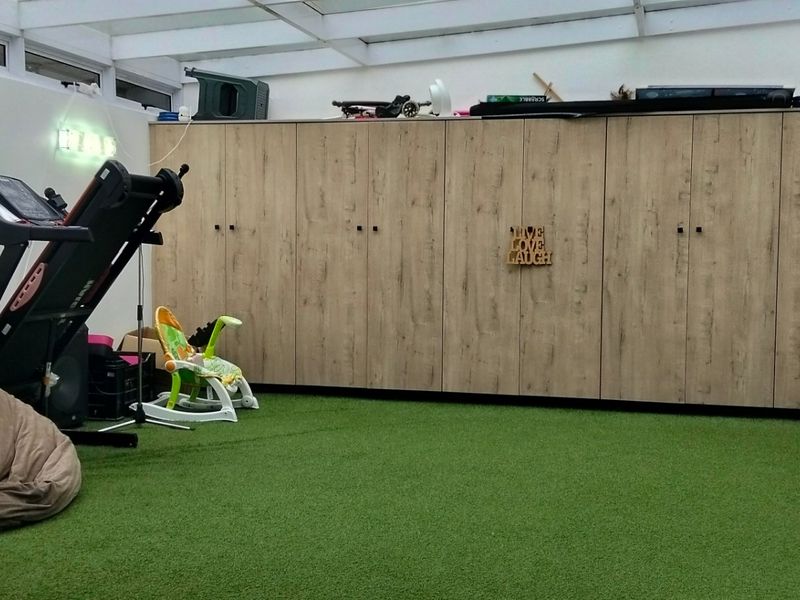A dedicated gym space featuring extensive built-in cabinetry, artificial grass flooring, and a bright glass roof structure.