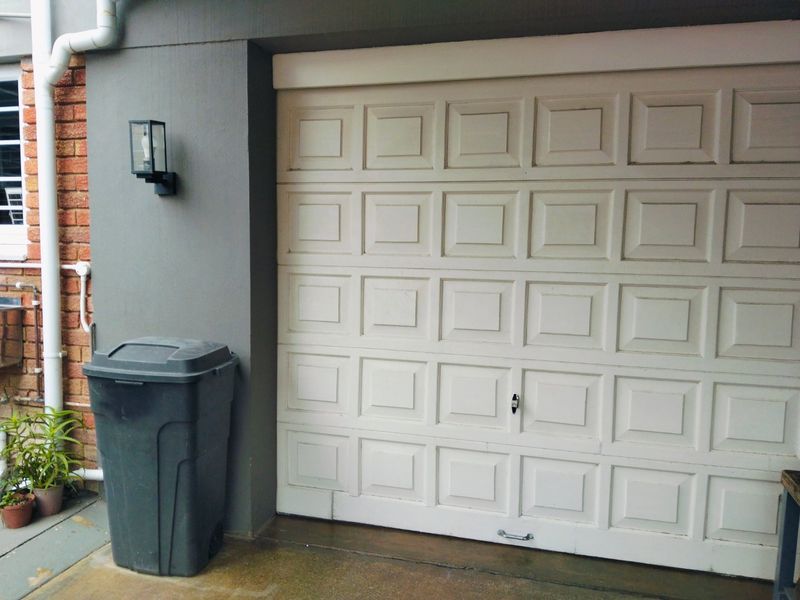 A view of a white sectional garage door set against a grey painted wall with exposed brick detailing and an exterior wall light.