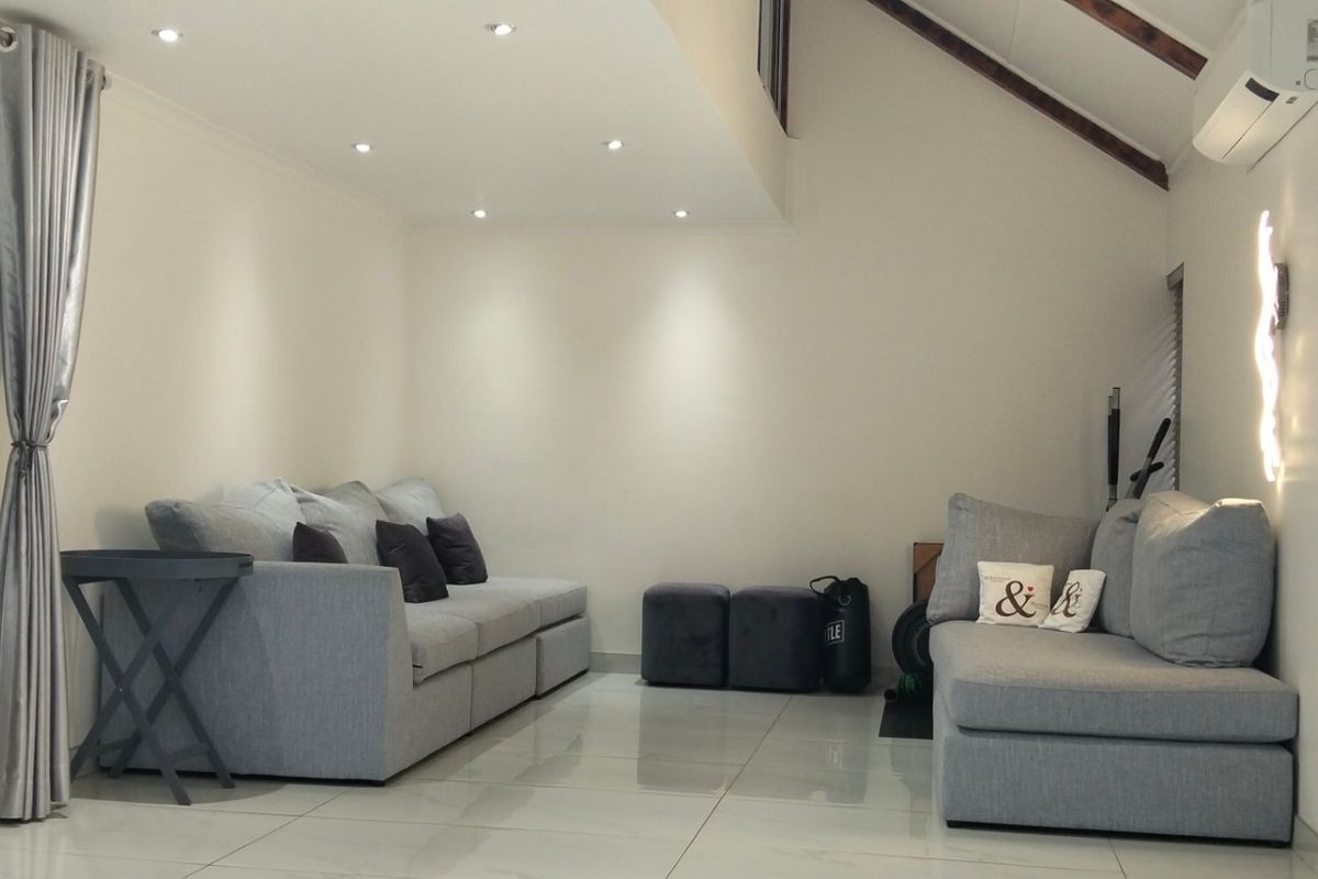 A bright living room featuring polished tiled floors, exposed timber rafters, recessed lighting, and a wall-mounted air conditioning unit.