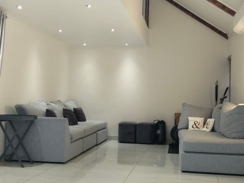 A bright living room featuring polished tiled floors, exposed timber rafters, recessed lighting, and a wall-mounted air conditioning unit.