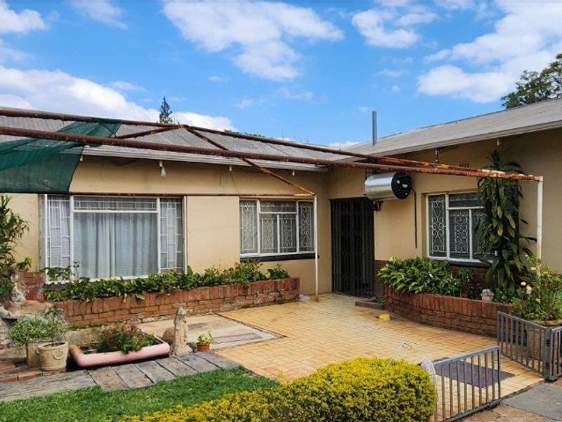 Rear exterior view featuring a paved patio area, brick planter boxes, and a metal pergola frame attached to the main dwelling structure.
