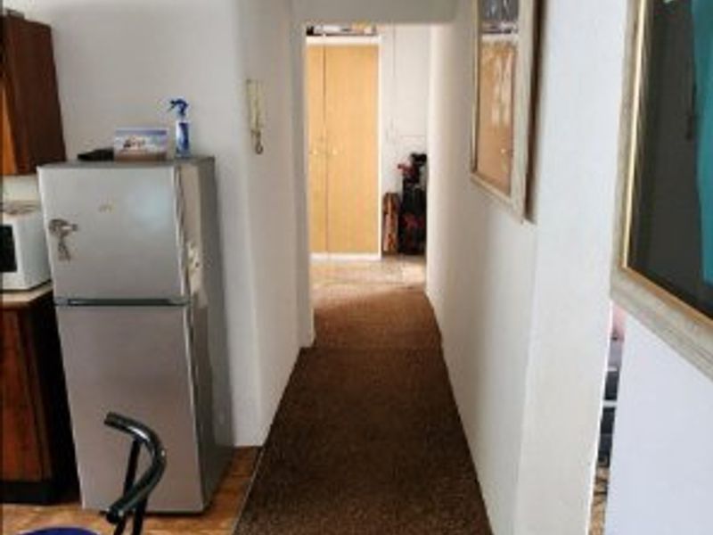 A narrow hallway featuring built-in storage cupboards and a tiled ceiling, showing signs of wear and requiring cosmetic updates.