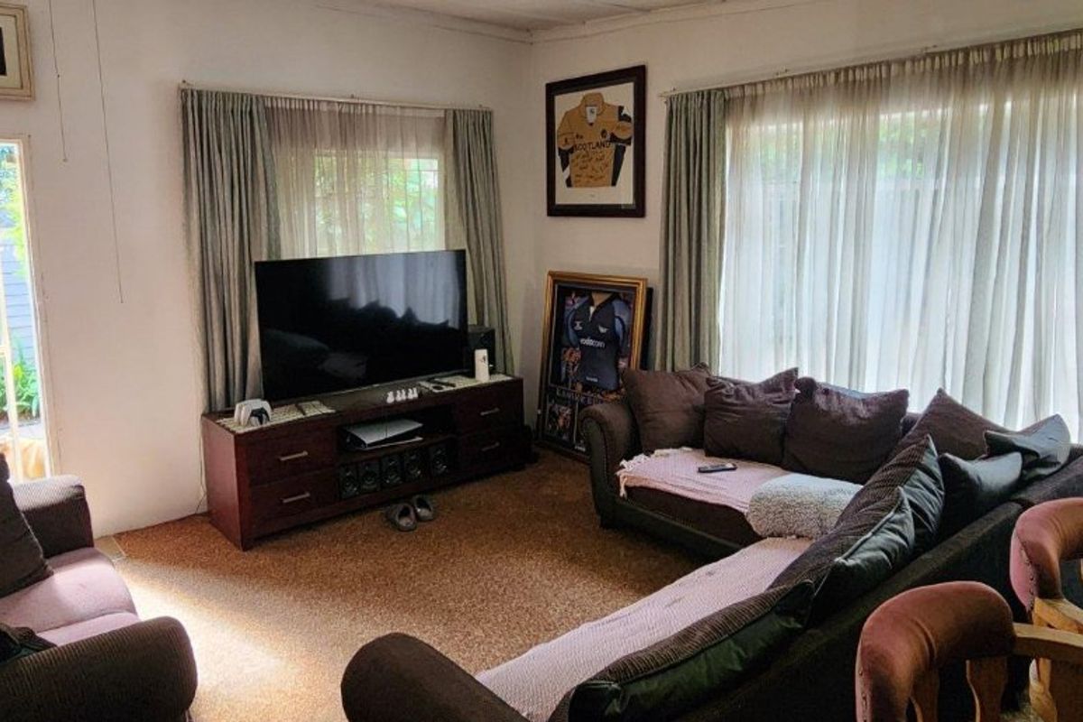 A living room featuring carpet flooring and large windows with curtains, providing access to the exterior through a sliding door.
