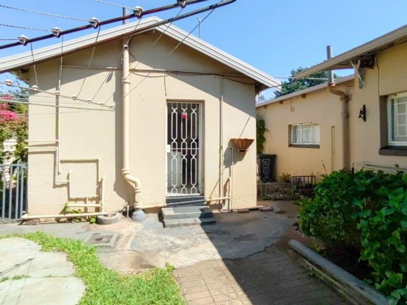 Rear exterior view of the property featuring a paved courtyard area, security gate, and external plumbing fixtures.