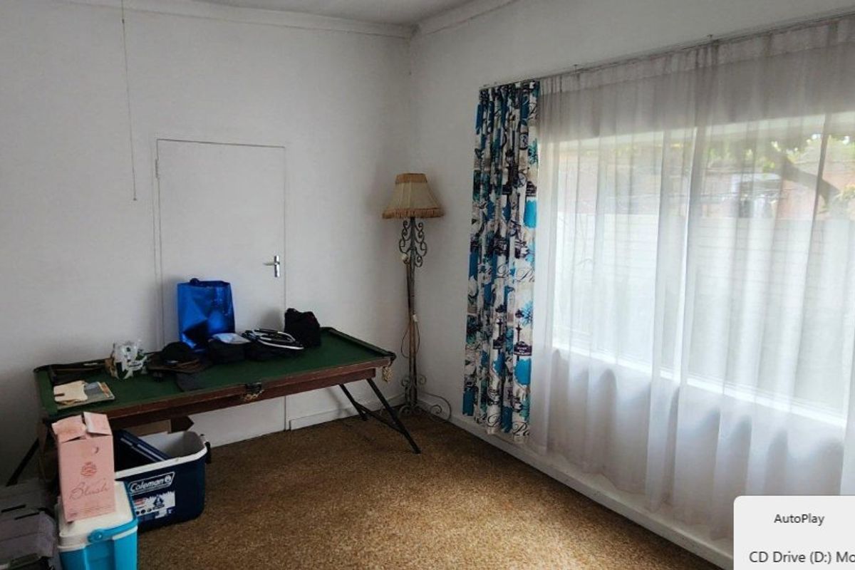 A bedroom featuring a large window with curtains and carpet flooring, offering a blank canvas for potential renovation and interior updates.