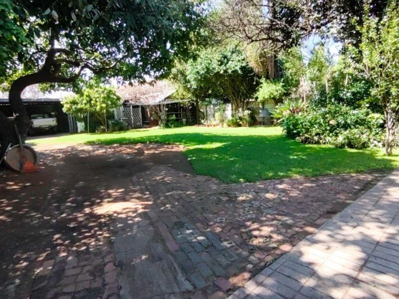 A spacious backyard garden featuring mature trees, a well-established lawn, and brick-paved pathways.