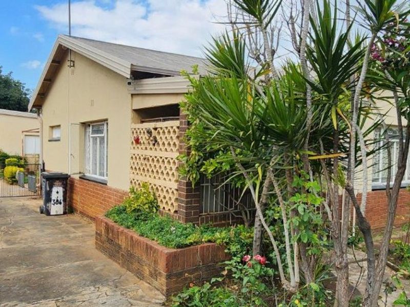 Front exterior view of a single-story house featuring a brick planter box, breeze block detailing, and a concrete driveway with security gate access.