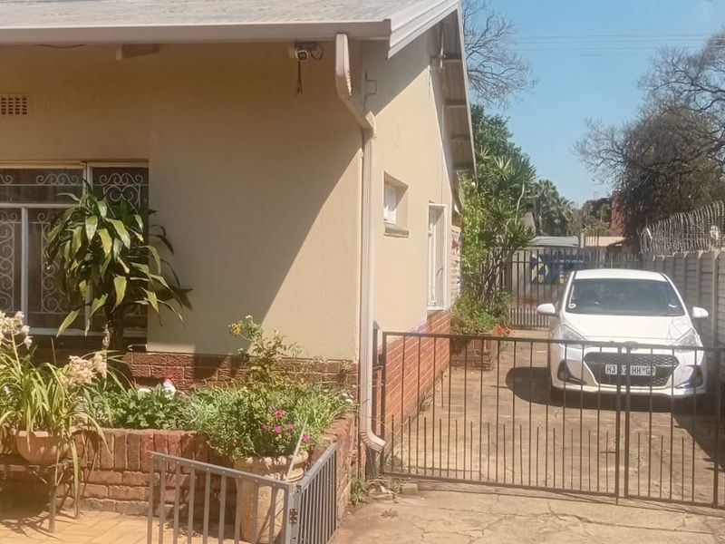 Front exterior view of the house featuring a paved driveway, security gate, precast boundary wall with razor wire, and a solar geyser installation.
