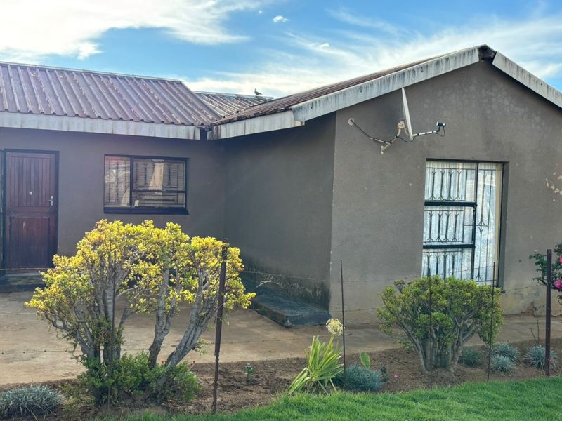 Rear view of the house featuring a corrugated metal roof, security bars on windows, and a concrete patio area.