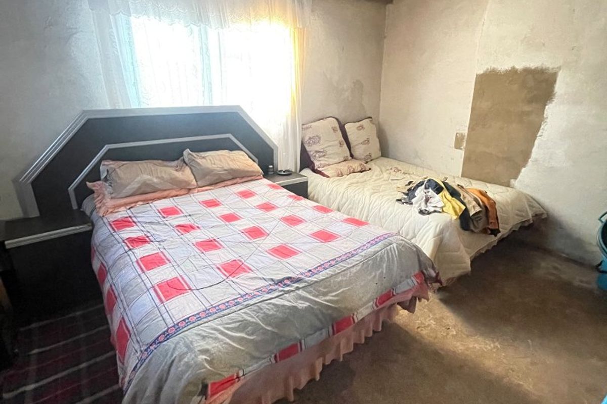 A bedroom featuring an exposed corrugated metal roof with timber rafters and a concrete floor, requiring significant finishing and renovation.