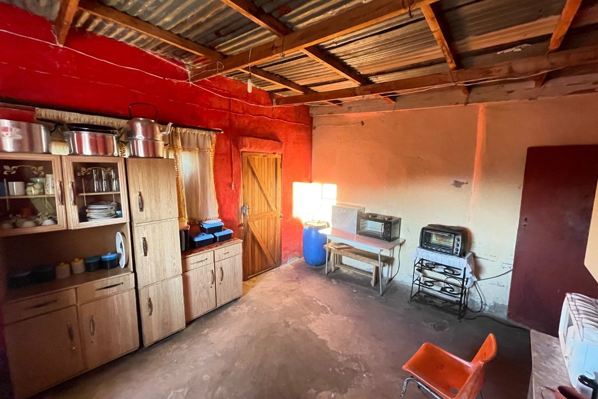 A rustic kitchen area featuring exposed timber roof trusses, corrugated metal ceiling, and basic wall finishes, offering significant potential for renovation and modernization.