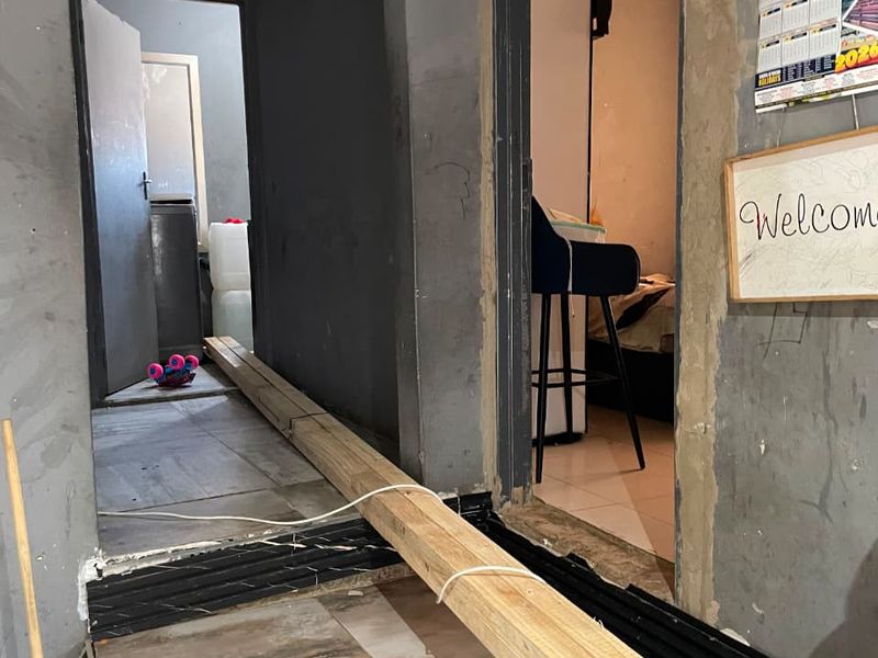 A hallway area currently under renovation with unfinished wall surfaces and exposed flooring transitions, requiring completion and cosmetic updates.