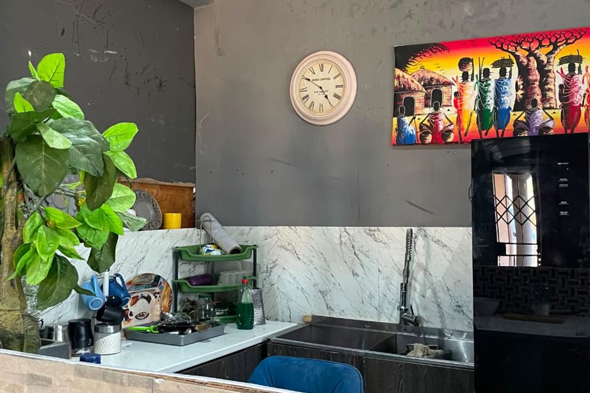 A compact kitchen area featuring a double bowl sink, marble-look backsplash, and a stone-clad breakfast bar, requiring cosmetic updates to the walls and ceiling.