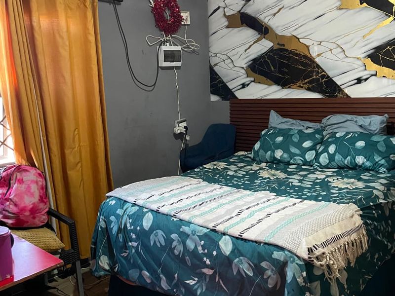 A bedroom featuring laminate flooring and a decorative wall panel behind the bed, currently requiring attention to exposed wiring and ceiling finishes.