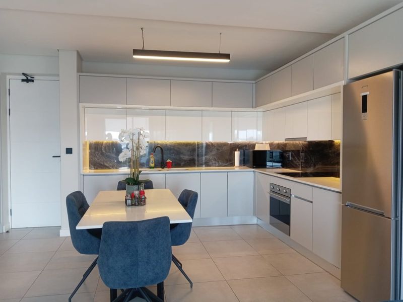 Modern open-plan kitchen featuring sleek white cabinetry, stone splashback, integrated appliances, and contemporary pendant lighting, seamlessly flowing into the dining area.