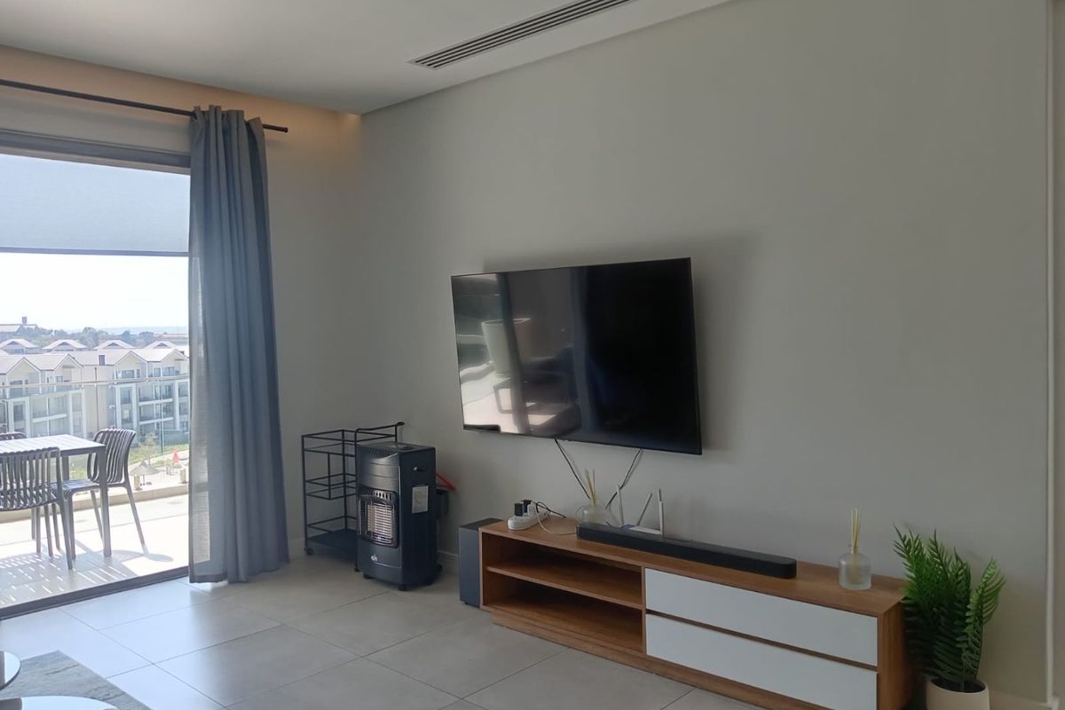 A bright living room featuring modern tiled flooring, ducted air conditioning, and a large sliding glass door providing access to an outdoor balcony.