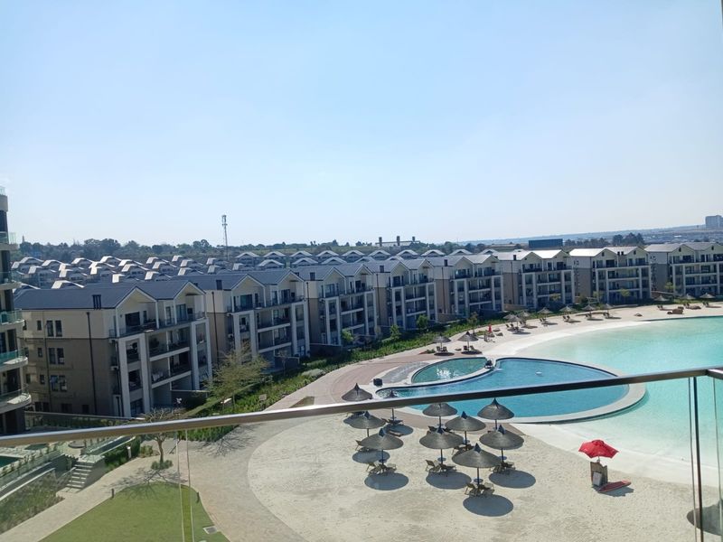 Elevated view overlooking a residential apartment complex featuring a large communal swimming pool, sandy beach area, and landscaped surroundings.