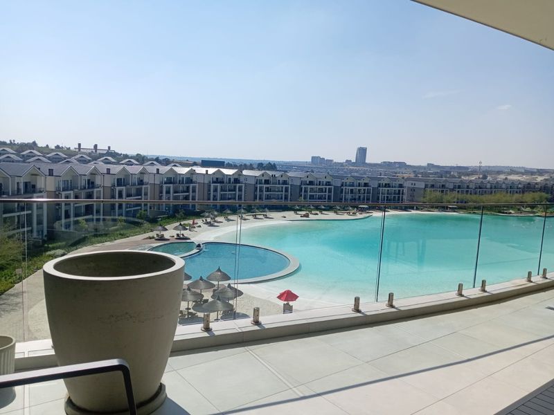 Spacious balcony with a modern glass balustrade, offering expansive views over the estate's swimming pool and surrounding residential complex.
