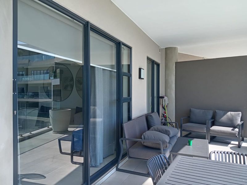 A spacious covered balcony featuring large sliding glass doors, modern tiled flooring, and a neutral color palette, ideal for outdoor relaxation.