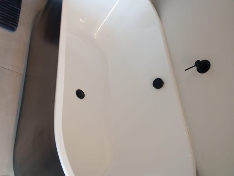 A modern bathroom featuring a sleek black and white freestanding bathtub with minimalist wall-mounted matte black tapware and neutral floor tiling.