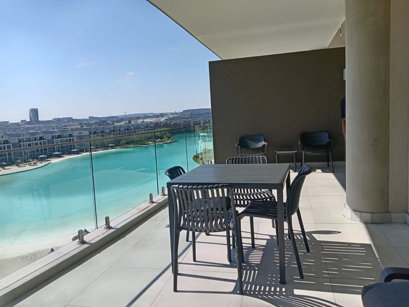 Spacious covered balcony featuring a modern glass balustrade and panoramic views of the lagoon and surrounding estate.
