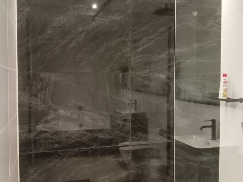 Modern bathroom featuring a spacious walk-in shower with a glass screen, rain shower head, and elegant dark marble-effect wall tiling.