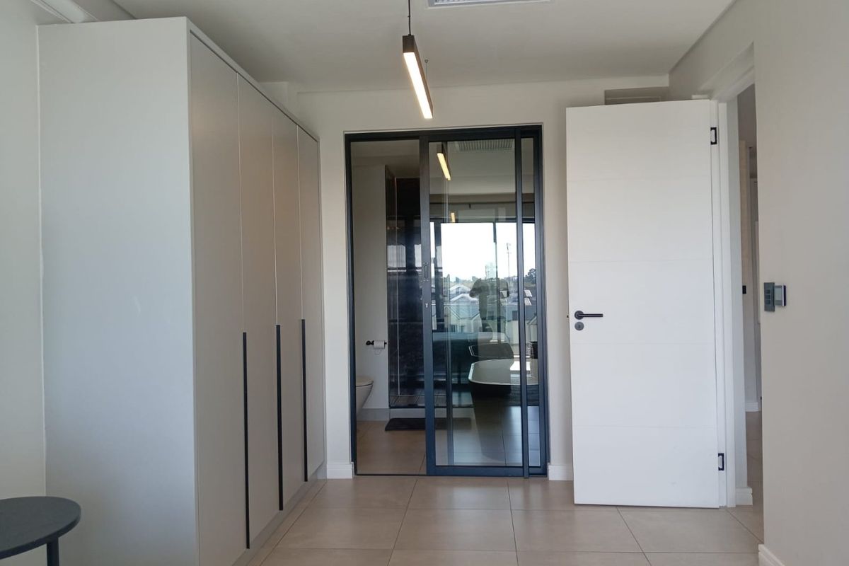 Modern bedroom featuring sleek built-in wardrobes, tiled flooring, and a contemporary glass partition leading to an en-suite bathroom.