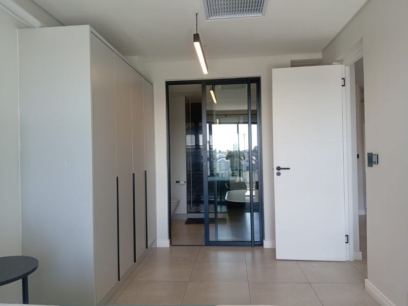 Modern bedroom featuring sleek built-in wardrobes, tiled flooring, and a contemporary glass partition leading to an en-suite bathroom.