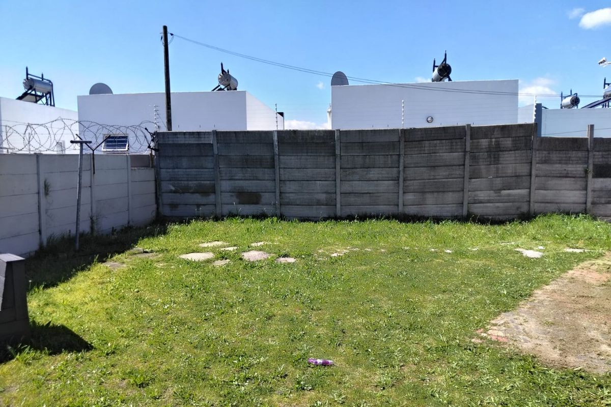 A rear garden area featuring a precast concrete boundary wall with electric fencing and visible solar water geysers on adjacent rooftops.