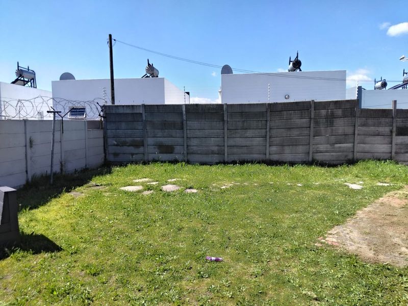 A rear garden area featuring a precast concrete boundary wall with electric fencing and visible solar water geysers on adjacent rooftops.