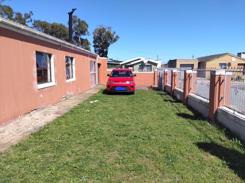 Front exterior view showing a driveway, perimeter wall with metal fencing, and the side facade of the house with visible paint wear.
