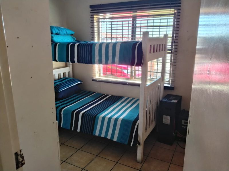 A compact bedroom featuring tiled flooring and a window with fitted venetian blinds.