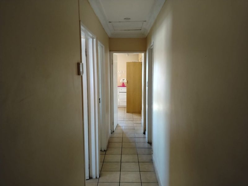 A functional hallway featuring tiled flooring and a ceiling access hatch, providing access to multiple rooms within the home.