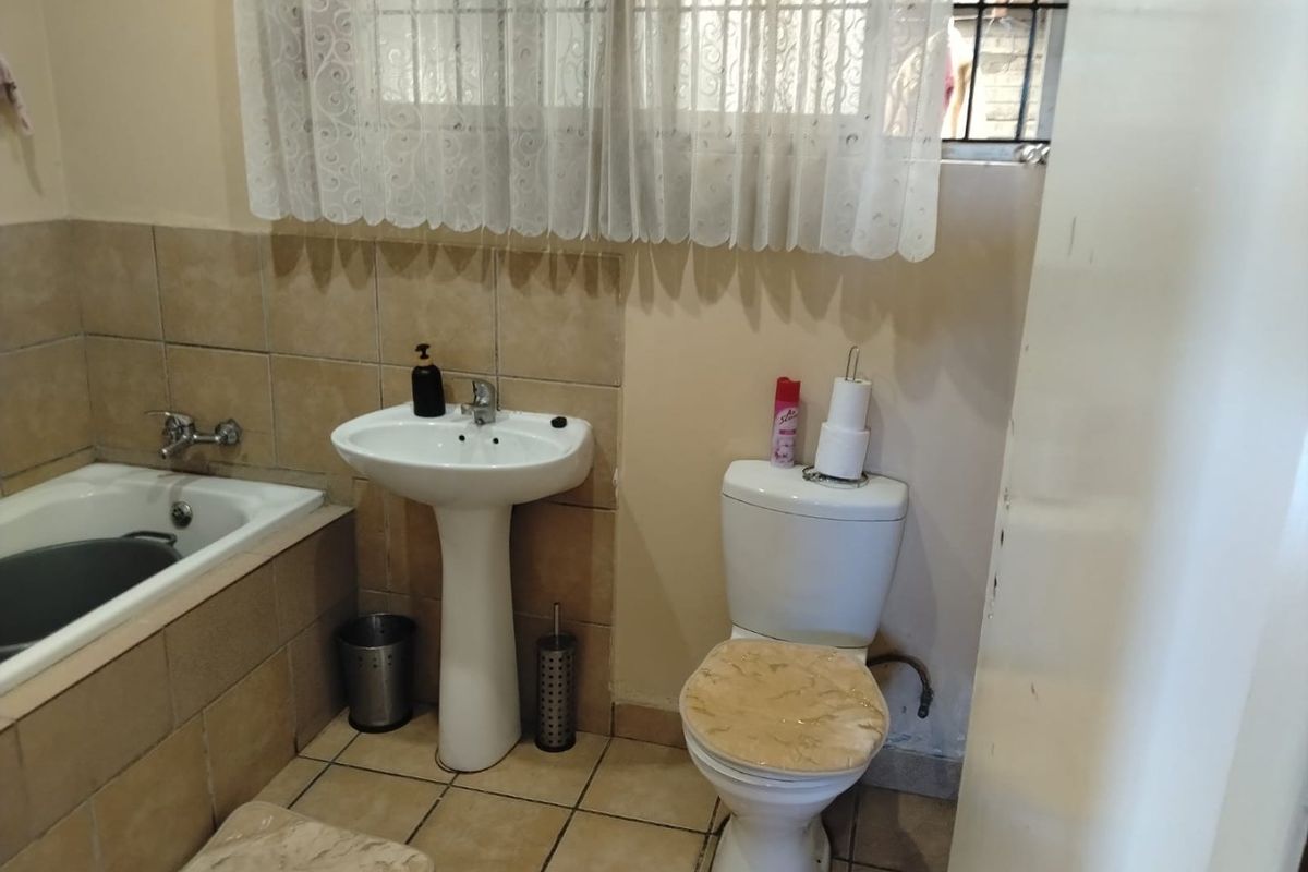 A functional bathroom featuring a pedestal basin, toilet, and built-in bathtub with tiled finishes, requiring cosmetic updates to improve its overall condition.