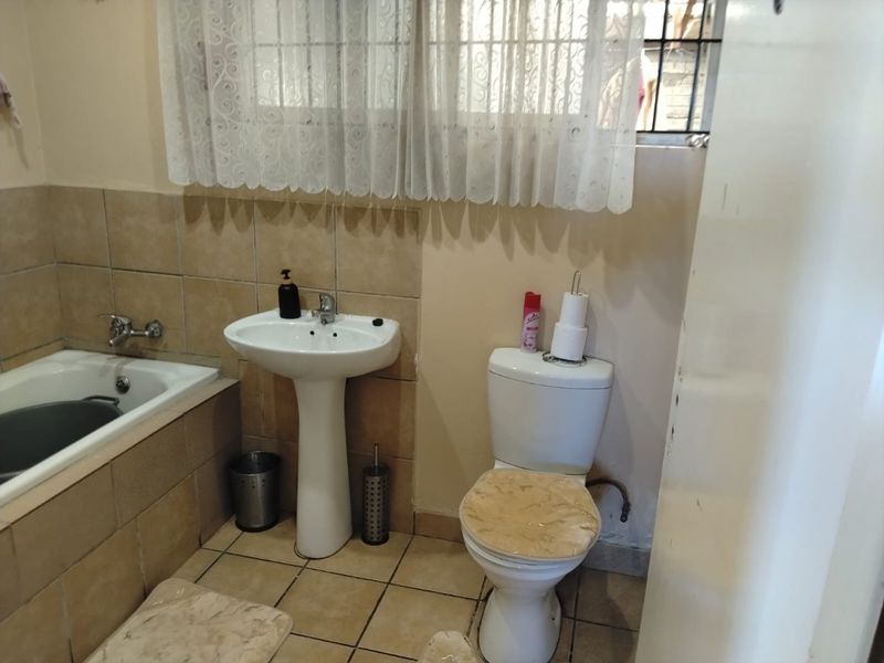 A functional bathroom featuring a pedestal basin, toilet, and built-in bathtub with tiled finishes, requiring cosmetic updates to improve its overall condition.