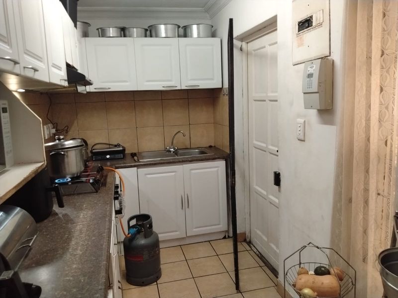 A functional scullery area featuring white built-in cabinetry, a double basin sink, tiled backsplash, and tiled flooring, providing practical utility space.